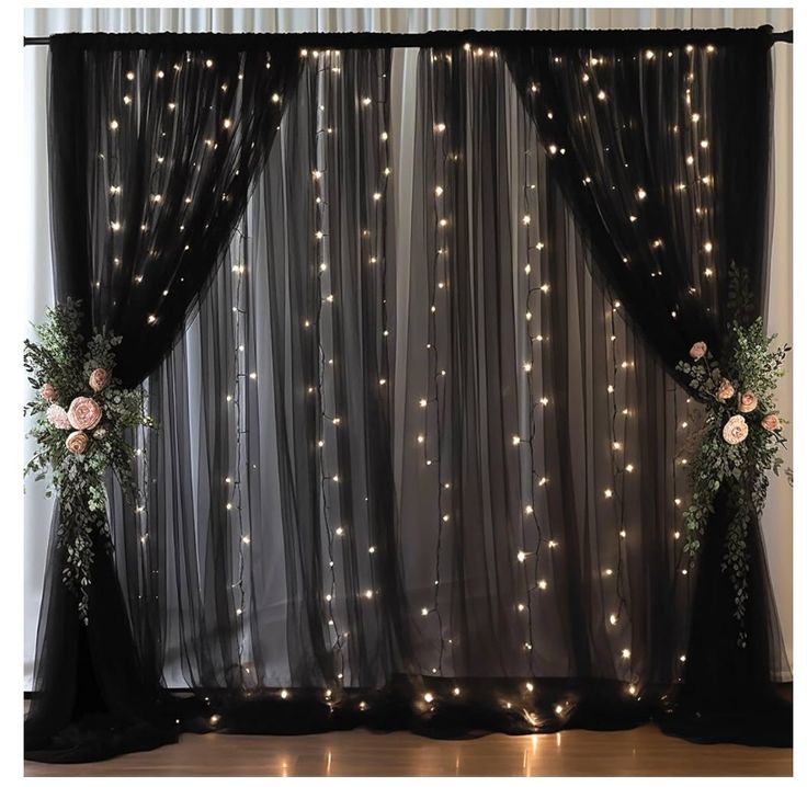 two vases filled with flowers sitting next to a window covered in sheer curtains and lights