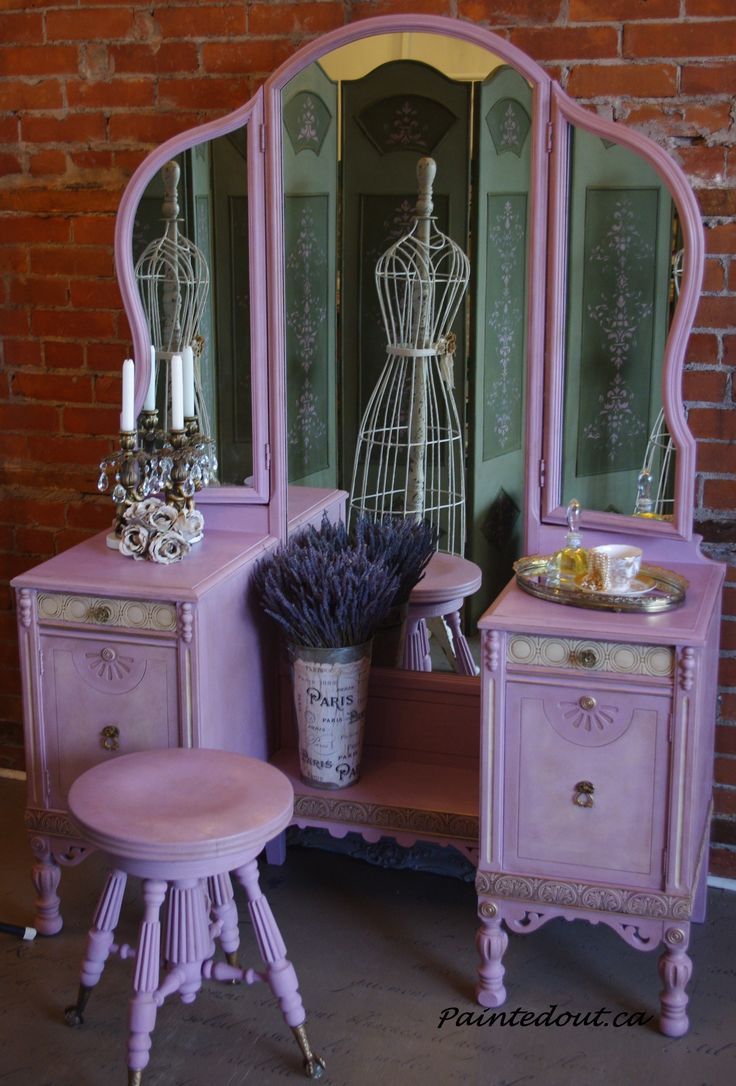 a pink vanity with mirror and stool next to brick wall