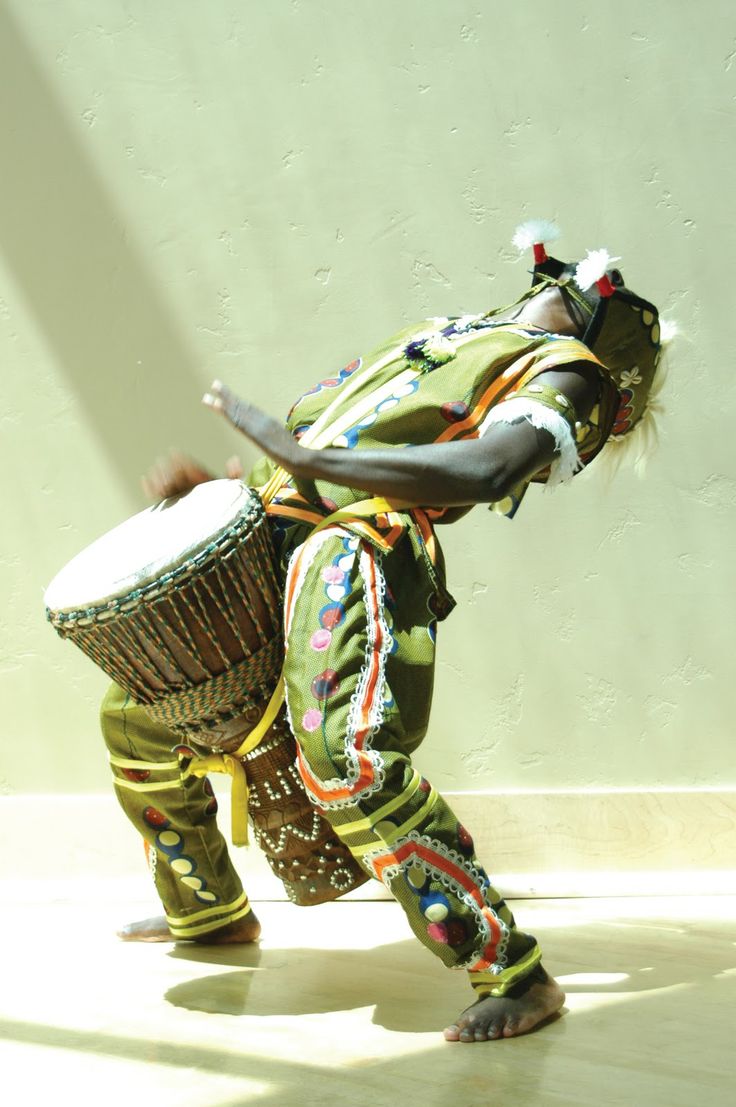 a woman in green and yellow outfit playing with a large drum while standing on the floor