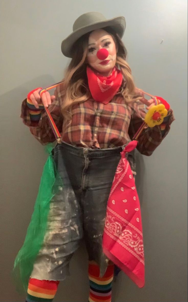 a woman dressed as a clown holding two umbrellas in her hands and standing next to a wall