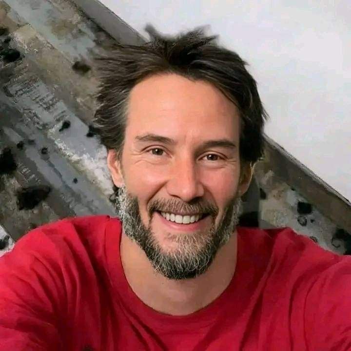 a man with a goatee smiles at the camera while wearing a red t - shirt