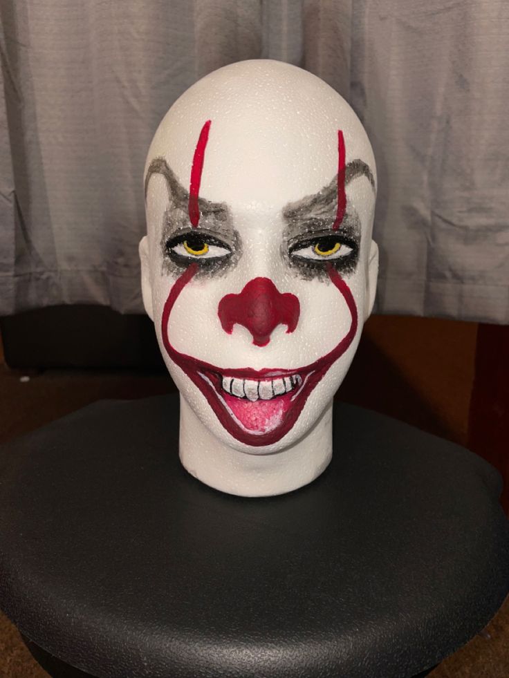 a white mask with red and black makeup on top of a table next to a curtain