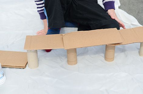 two people are sitting on the ground with cardboard boxes in front of them and one person is holding a skateboard