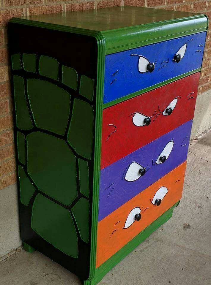 a multicolored chest of drawers with eyes painted on the front and sides, sitting next to a brick wall