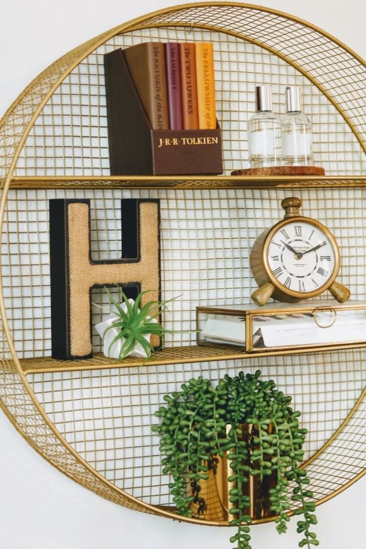 a gold shelf with books, plants and a clock on it's side next to a potted plant