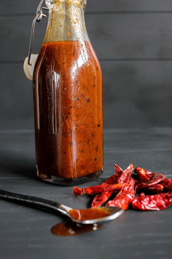 a bottle filled with sauce next to some chili peppers and a spoon on the table