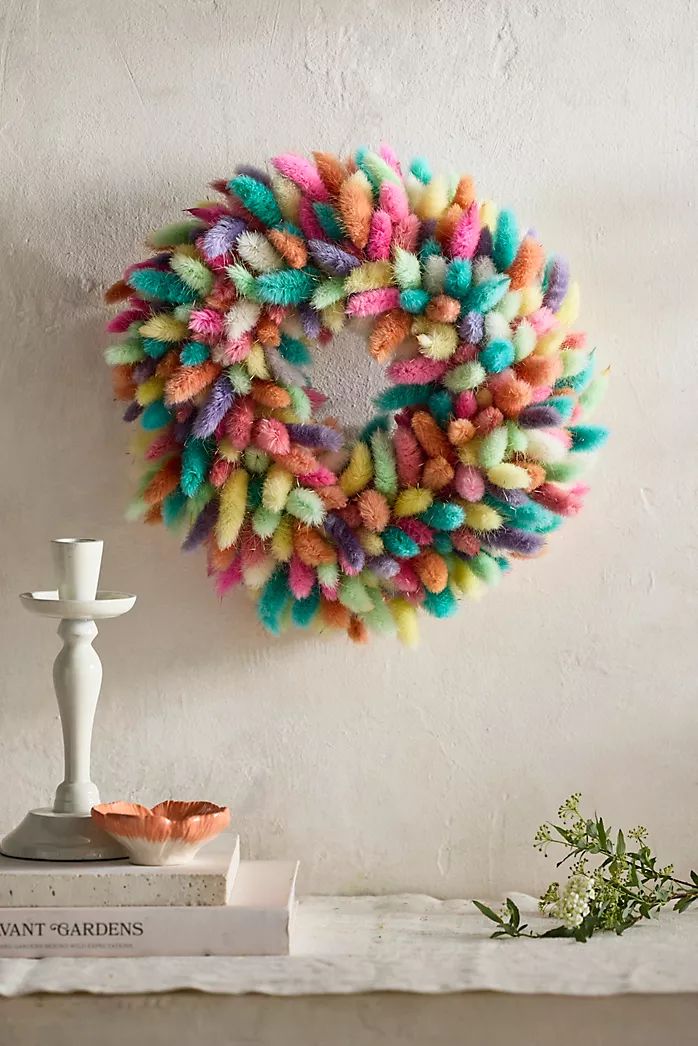 a multicolored wreath hanging on the wall next to a candle and some books