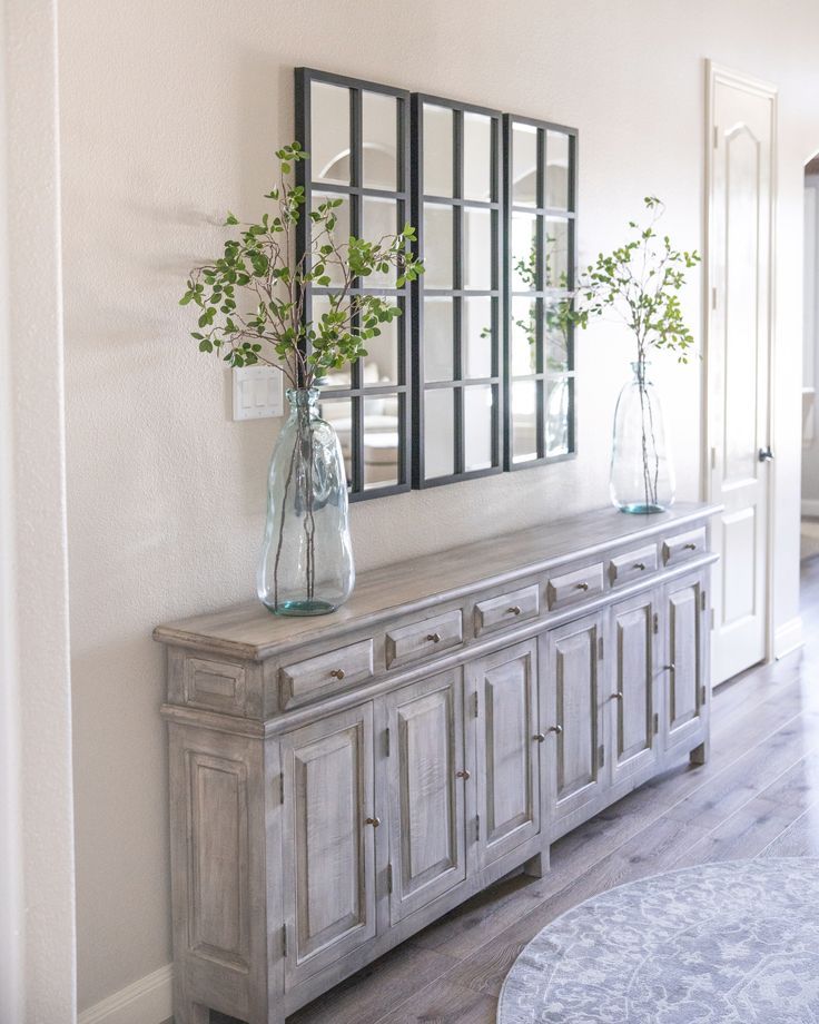 a vase with flowers sitting on top of a wooden dresser next to a mirror and door