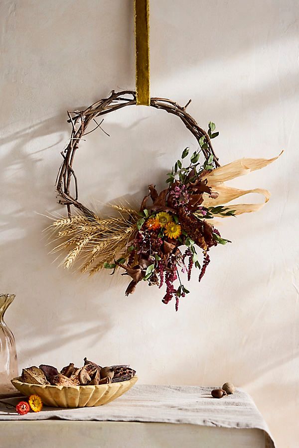 a wreath with dried flowers and leaves hanging on the wall next to a bowl of food