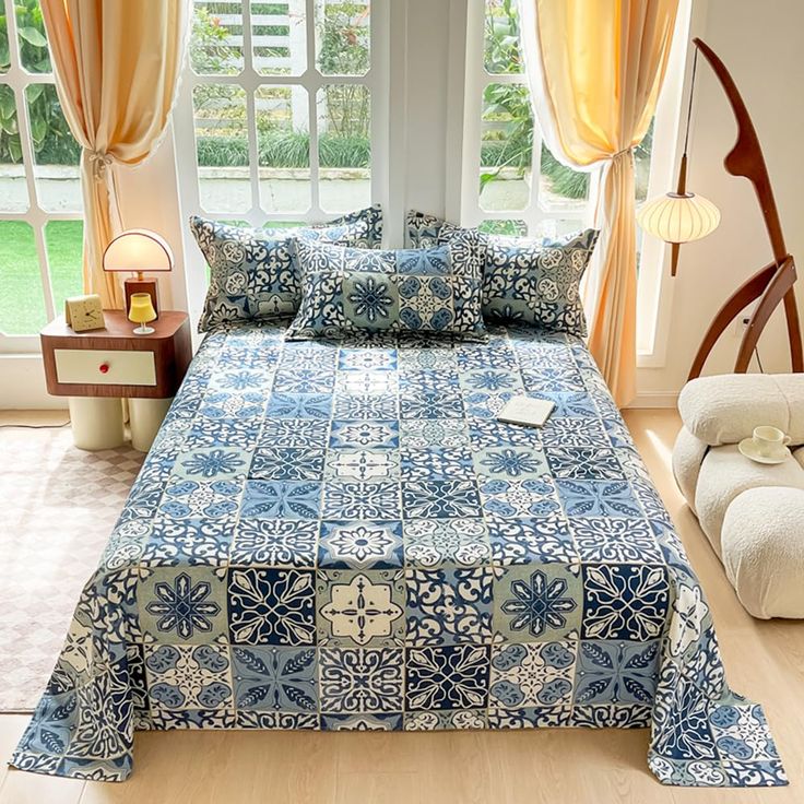 a blue and white bed in a bedroom next to a window with yellow drapes