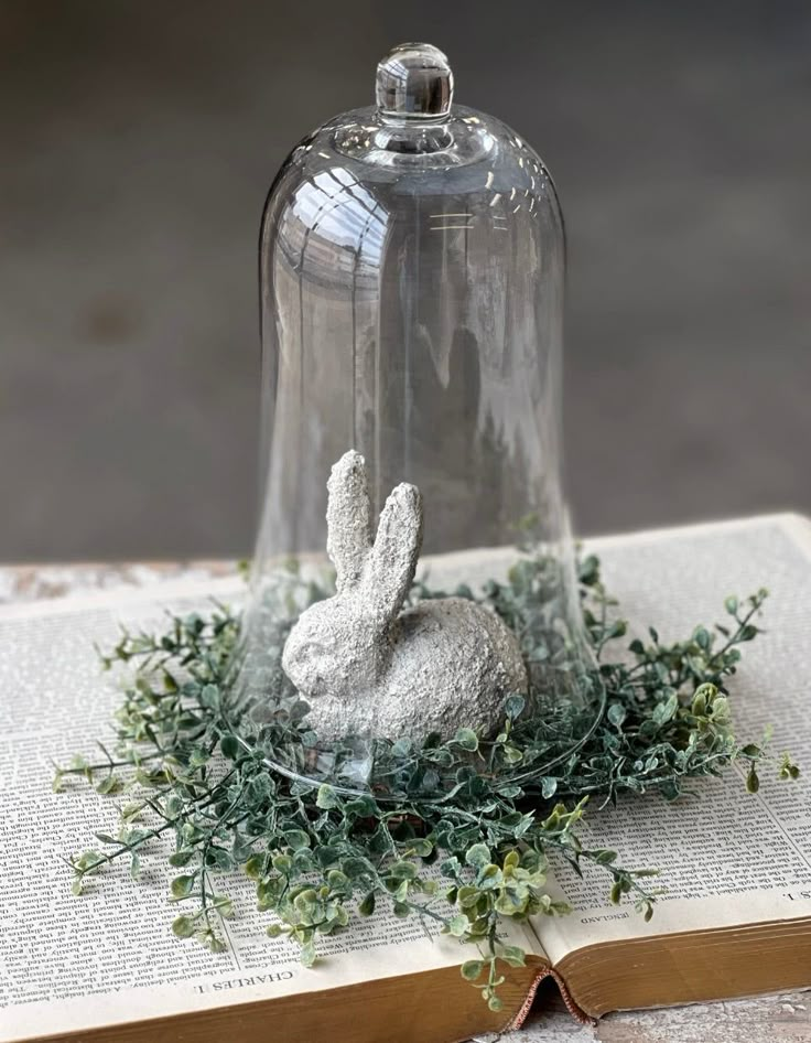 a glass bell jar sitting on top of an open book next to a bunny figurine