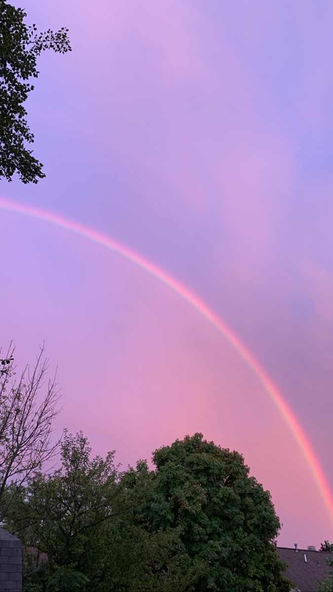 two rainbows in the sky over some trees and houses at sunset or sunrise time