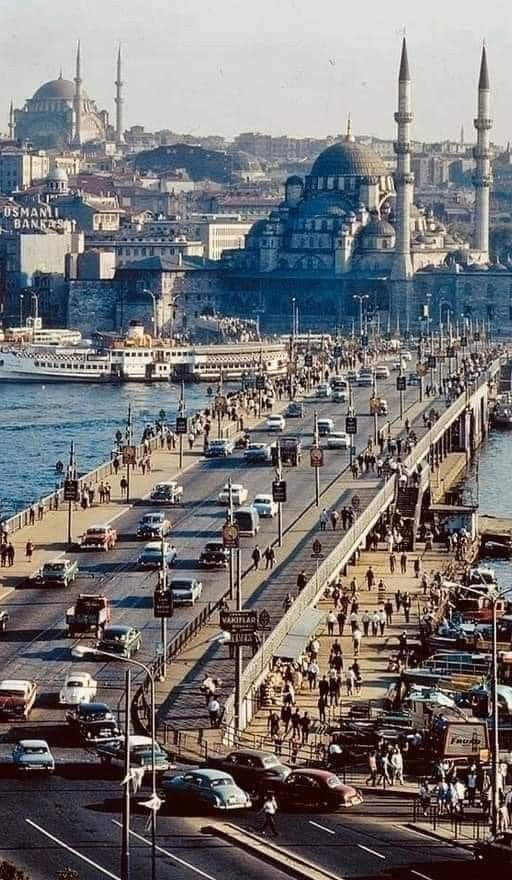 an old photo of a busy street with cars and people walking on the sidewalk next to the water