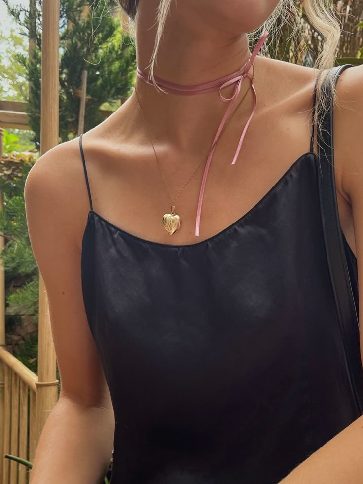 a woman with blonde hair wearing a black top and pink leather choker is looking at the camera