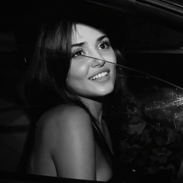 a black and white photo of a woman in a car smiling at the camera with her eyes closed