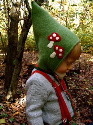 a young child wearing a green hat with mushrooms on it's head in the woods