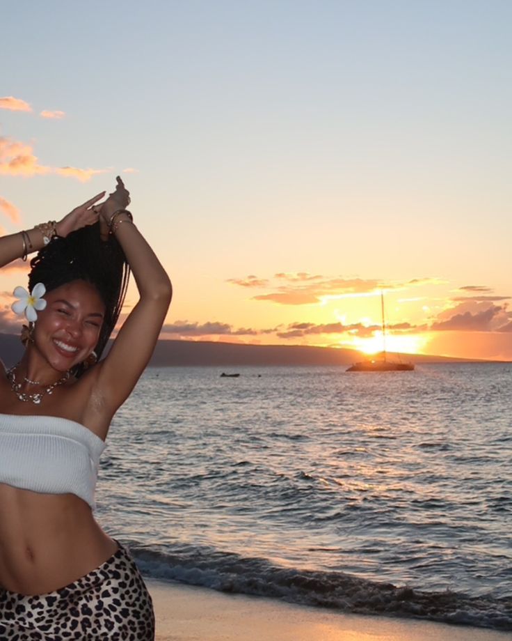 a woman standing on top of a sandy beach next to the ocean at sun set