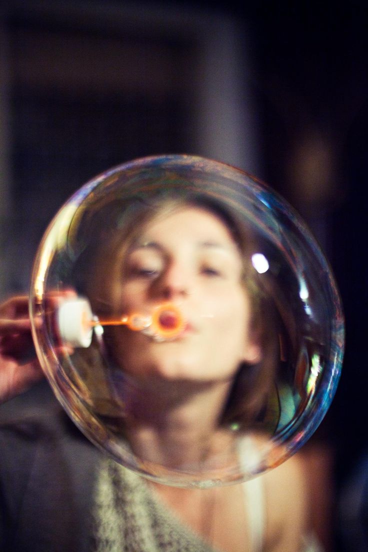 a woman blowing bubbles into the air with her eyes closed