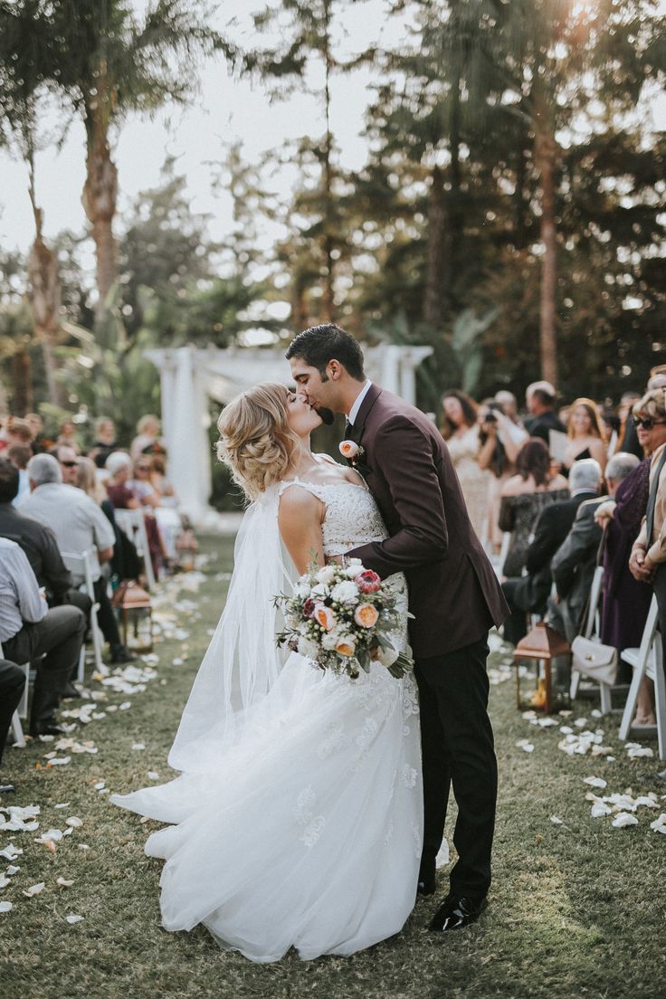 a bride and groom kissing in front of an audience at their outdoor wedding ceremony on the lawn