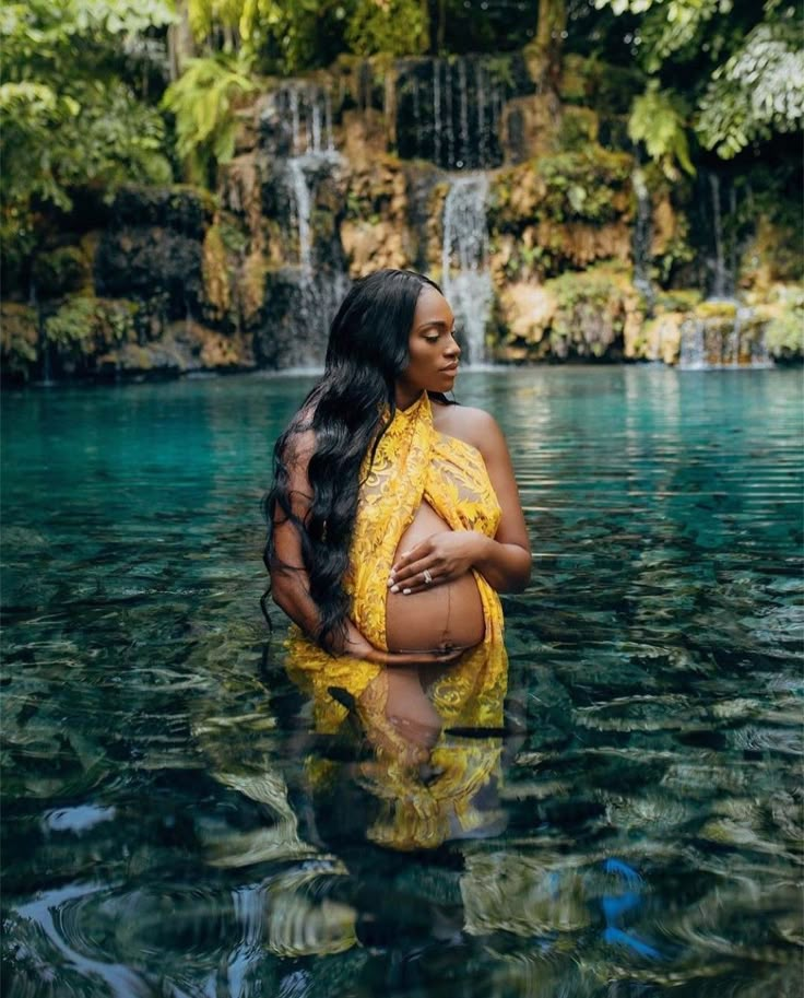 a pregnant woman standing in the water near a waterfall