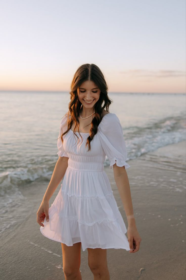 a woman standing on top of a sandy beach next to the ocean wearing a white dress