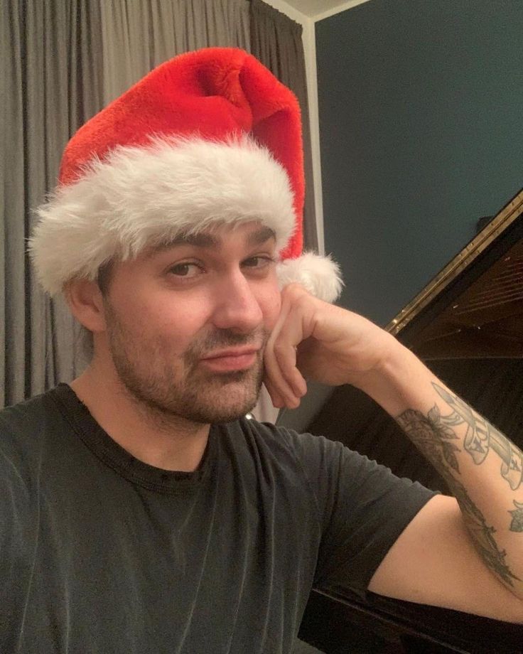 a man wearing a santa hat while sitting in front of a piano and looking at the camera