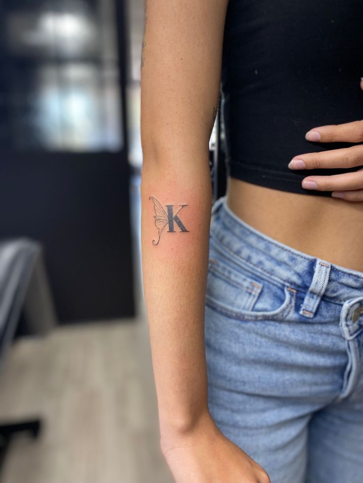 a woman with a tattoo on her left arm and the letter k behind her back