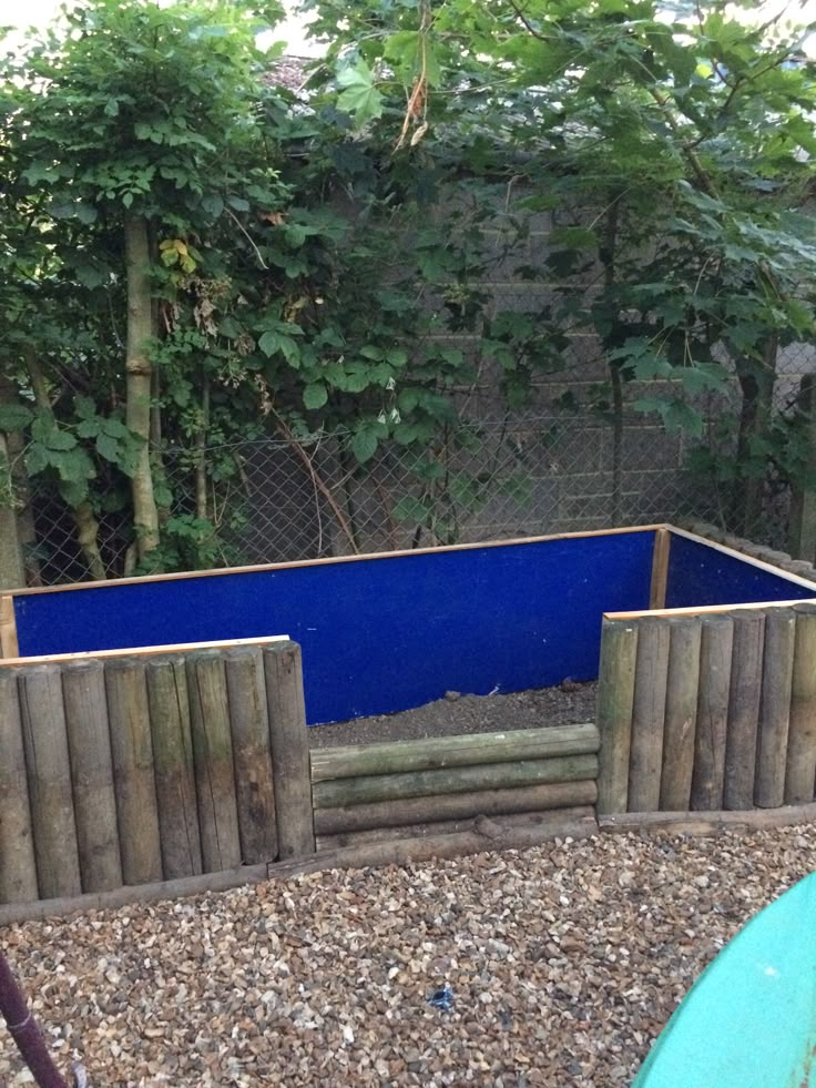 a blue pool in the middle of a gravel area next to a fence and trees