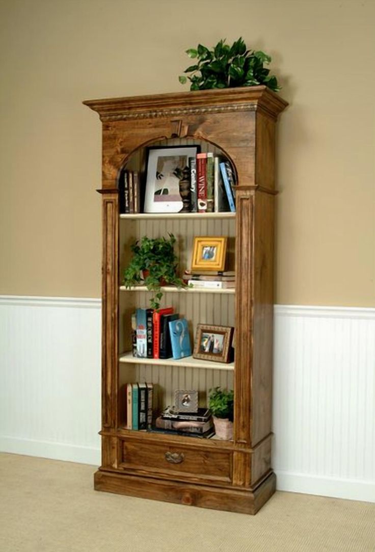 a wooden bookcase with books and plants on top in a living room next to a wall