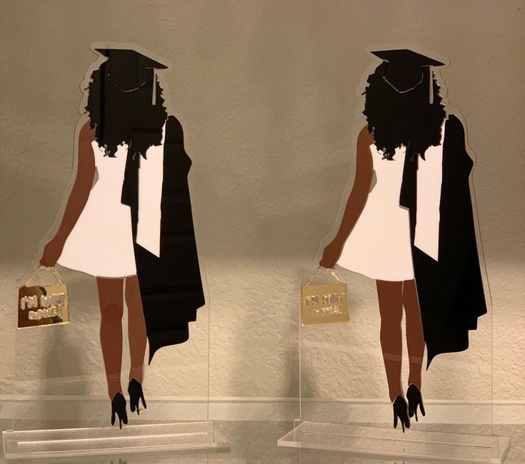 two acrylic cutouts of black women in graduation caps and gowns, one holding a gold purse