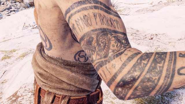 a man with tattoos on his arm and leg is standing in the snow near rocks