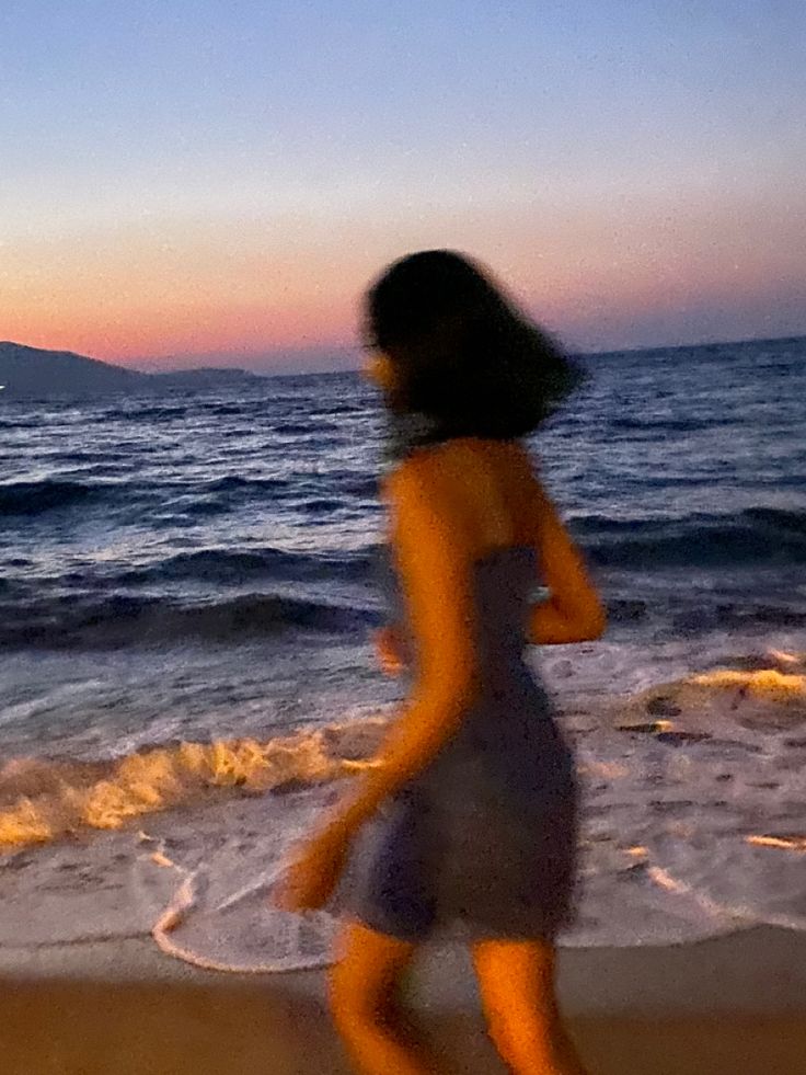 a blurry photo of a woman walking on the beach at sunset with waves coming in