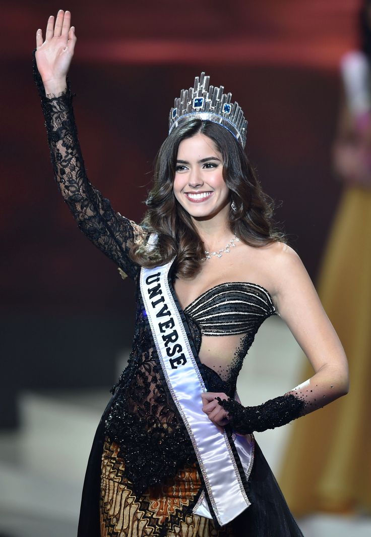 a woman in a black and gold dress waves to the crowd while wearing a tiara