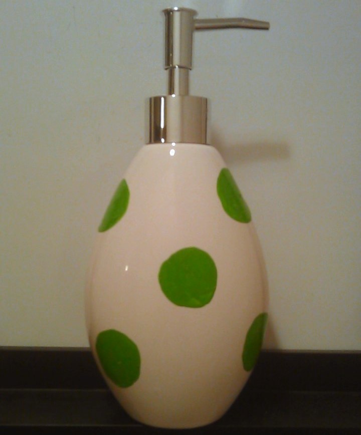 a white and green soap dispenser with polka dots on it sitting on a counter