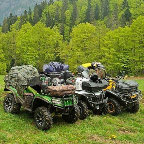 four atvs are parked on the grass in front of some mountains and trees with backpacks on them