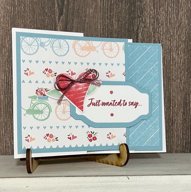 a close up of a greeting card on a wooden surface with a bicycle and flowered background