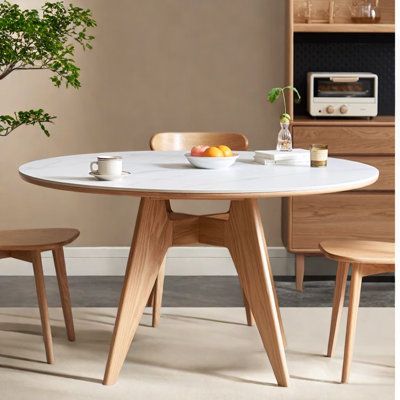 a white table with two wooden chairs and a potted plant in the corner next to it