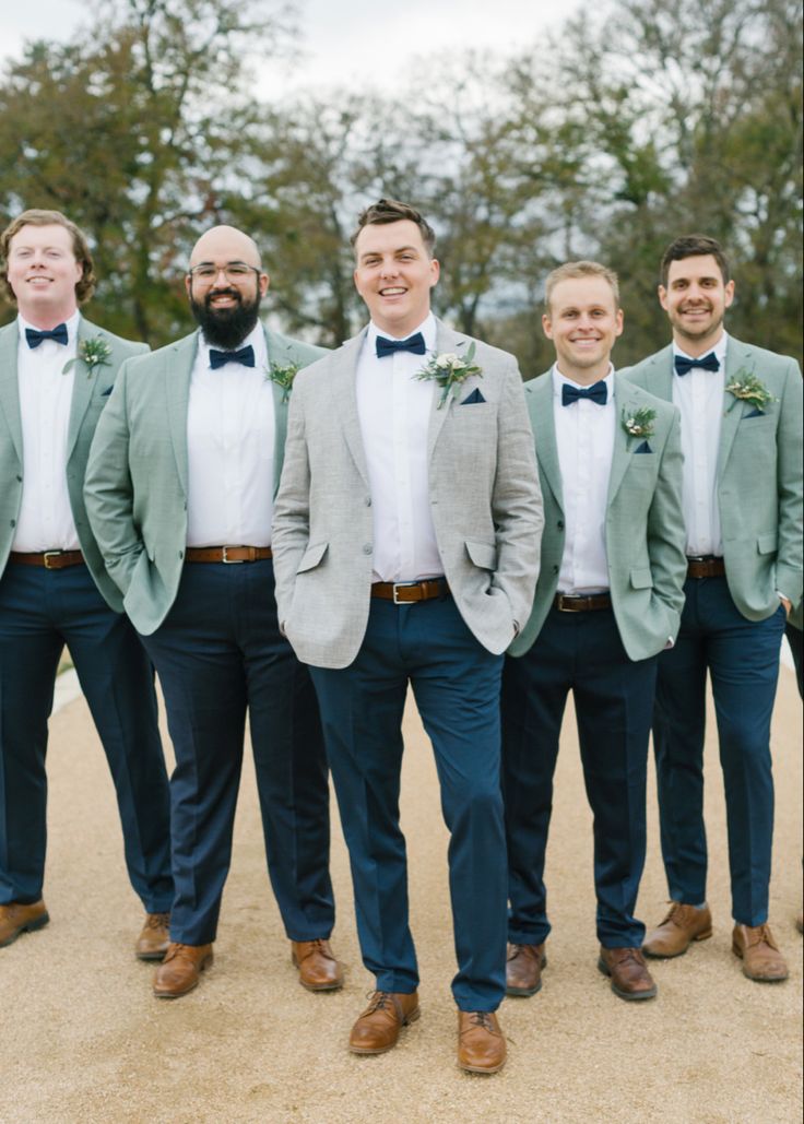 a group of men standing next to each other wearing suits and bow ties with trees in the background