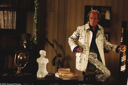 a man in white jacket sitting on top of a wooden table next to a lamp