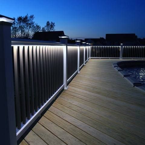 a wooden deck with white lights on it at night, next to a pool and fence