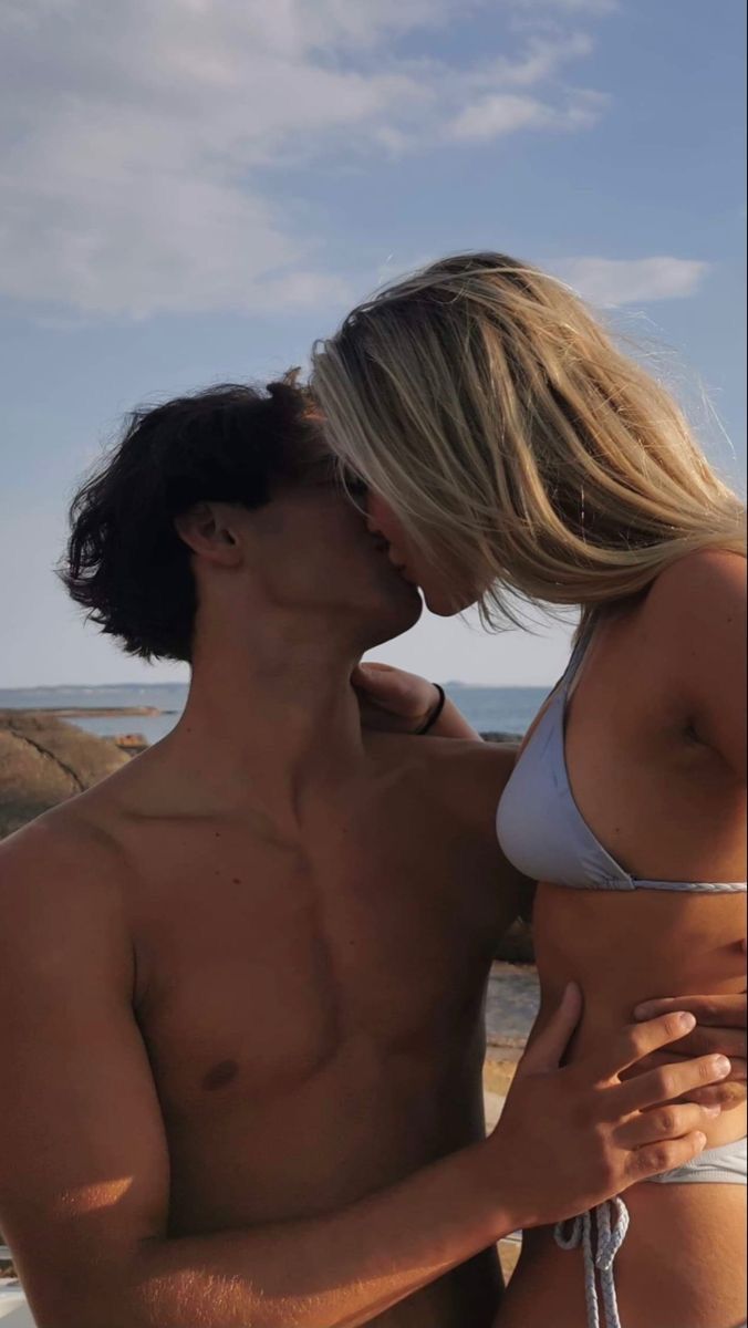 a man and woman kissing on the beach next to the ocean in swimsuits