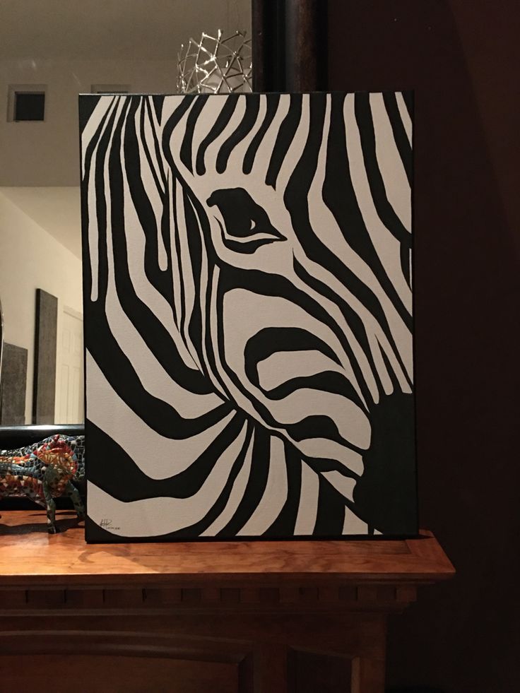 a black and white zebra painting sitting on top of a wooden table next to a mirror