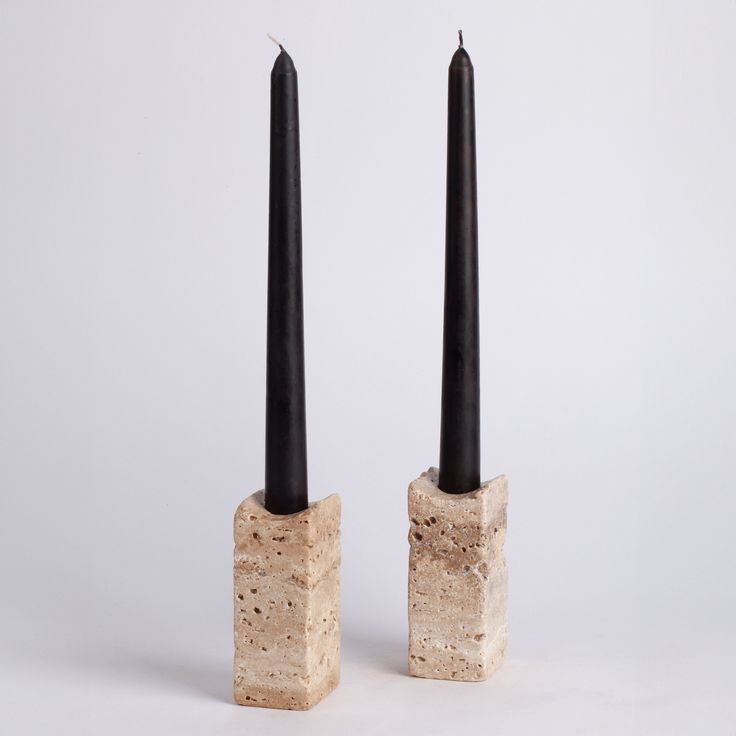 two black candles sitting on top of each other next to each other in cement blocks