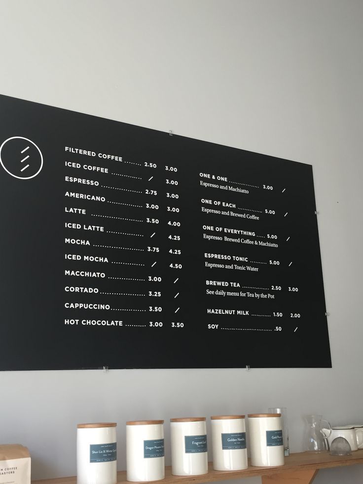 the menu is hanging on the wall above the coffee shop's counter top, along with several cups