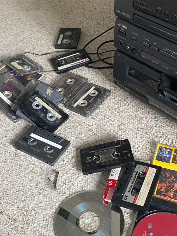 an assortment of old and used cassettes on the floor next to a cd player