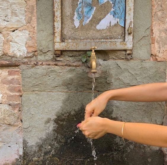 a woman is washing her hands with water from a faucet in front of a stone wall