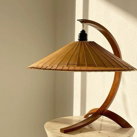 a wooden lamp sitting on top of a table next to a white wall and window