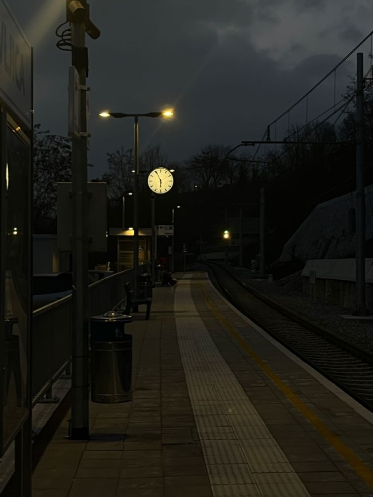 a train station at night with a clock on the platform and lights in the dark