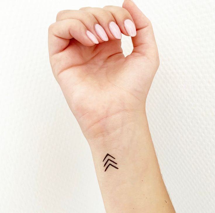 a woman's arm with a small black arrow tattoo on the left side of her wrist