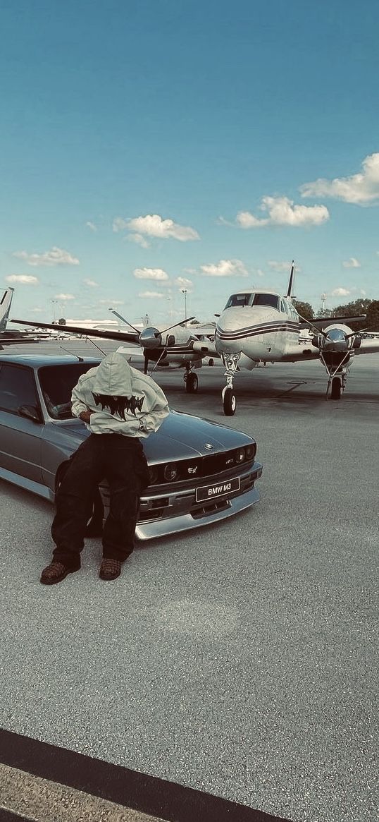 a man sitting on the hood of a car in front of an airplane